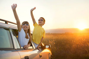 Two smiling kids waving from parked car during sunset